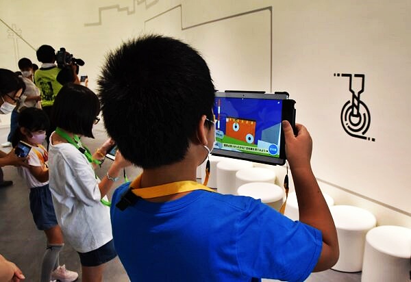 壁にデザインされたARマーカーにタブレットをかざす子どもたち。AR動画で電気のしくみを学ぶことができる