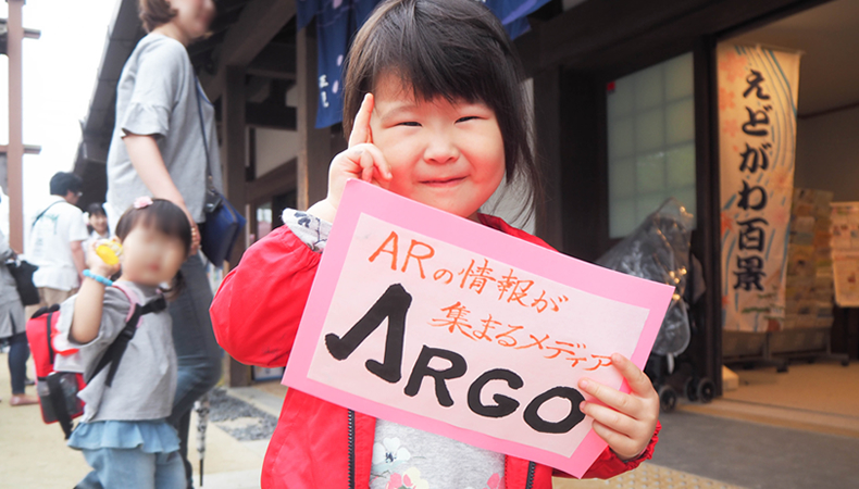 習字で「ARGO」と書いた作品を持ってピースサインをする娘