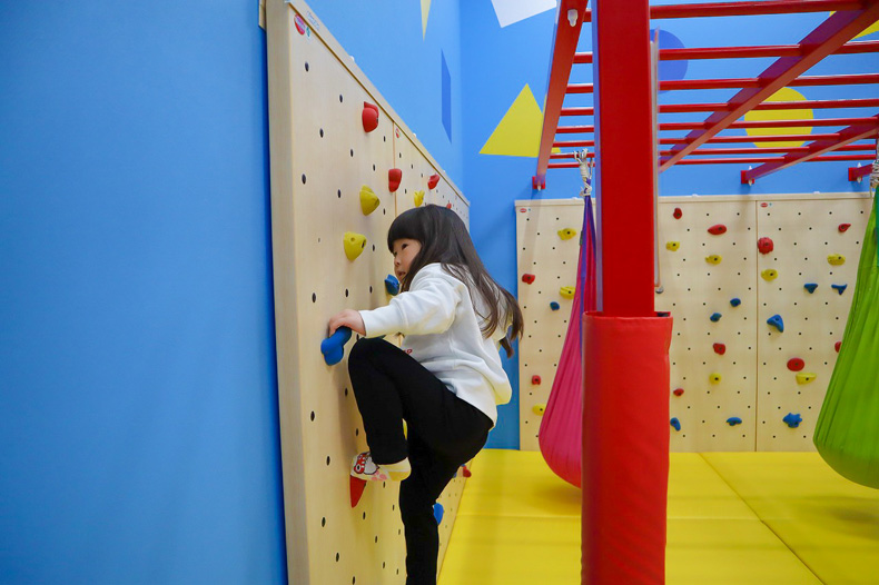 ボルダリングの壁を、一生懸命上へ上へ登ろうとする娘を横から撮影