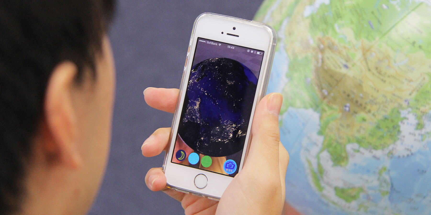 地球儀「ほぼ日のアースボール」を専用アプリで読み取り、夜の地球を観察する子ども