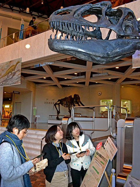 音声ARの説明パネルの前で巨大な骨格標本を見上げる博物館来館者