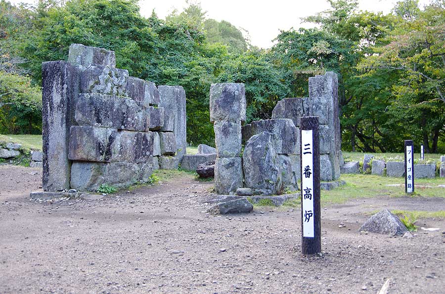 石が積まれた世界文化遺産の「橋野鉄鉱山」。「三番高炉」と「フイゴ座跡」の長細い看板が立てられている